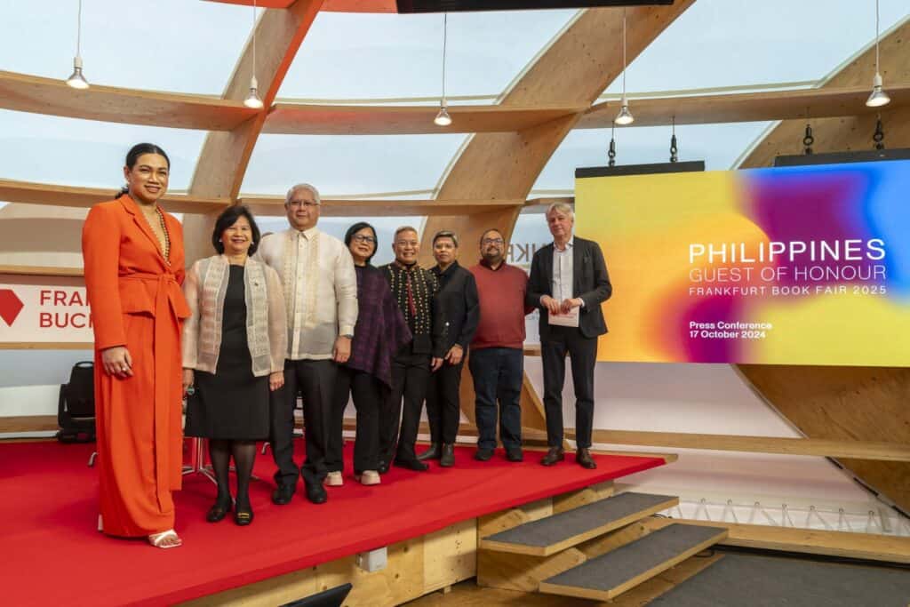 A group of seven people standing on a red stage at a press conference for the Frankfurt Book Fair 2024, with a screen announcing the Philippines as the Guest of Honour for 2025.