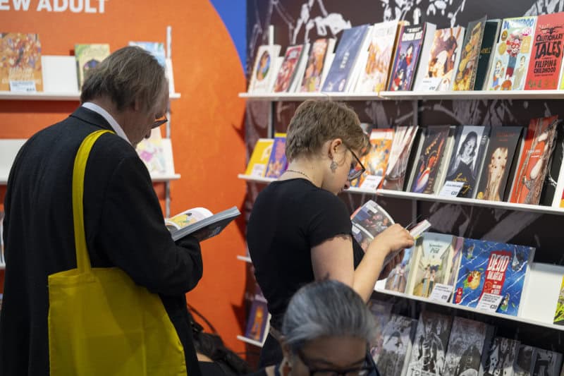 Two people standing and browsing graphic novels on display shelves at the Leipzig book fair