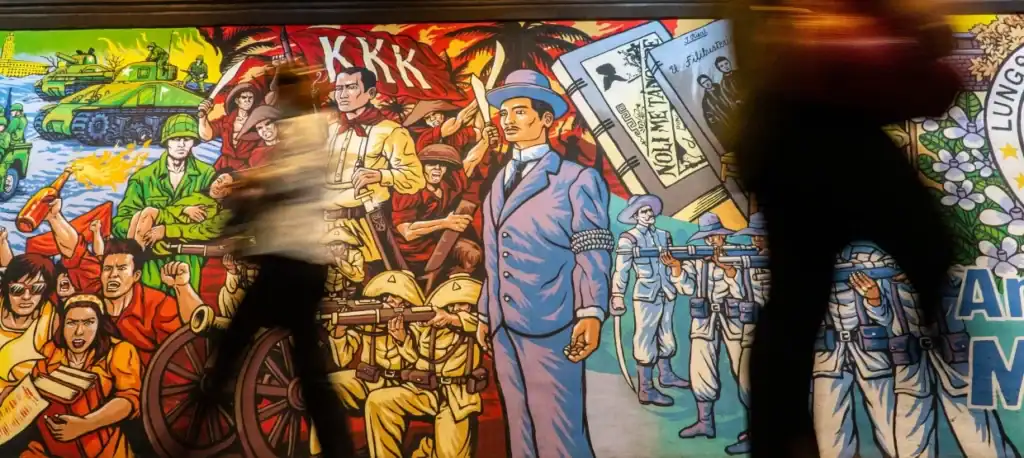 People walk past a colorful mural depicting historical and controversial figures like Jose Rizal and Andres Bonifacio