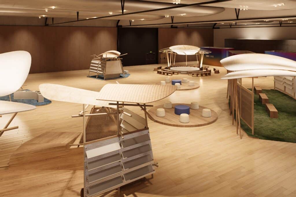 An indoor exhibit space with wooden floors featuring abstract, wing-like sculptures, small stools, and circular seating arrangements under soft lighting.