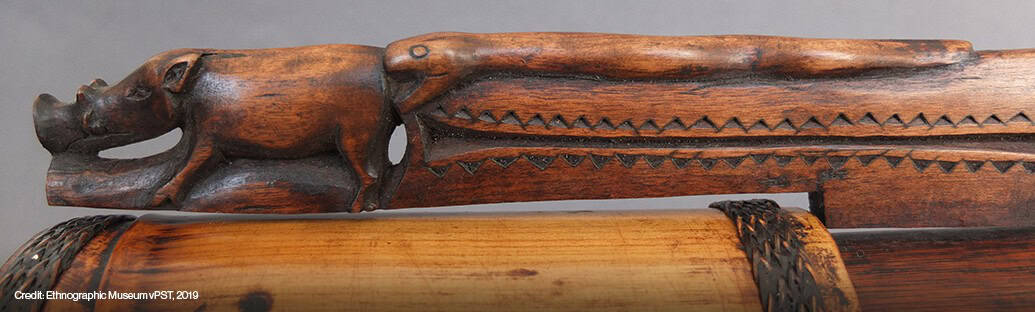 Close-up of a carved wooden object featuring a snake and a pig, with decorative patterns along the side.
