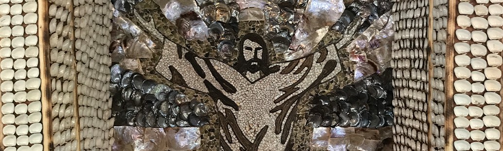 A mosaic depicting a figure of Jesus with arms raised, created using various stones and shells set in a rectangular frame.